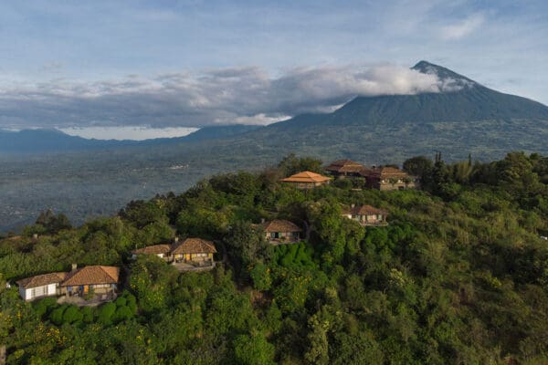 Press 1 Aerial view of Virunga Lodge with lush greenery and the Virunga Volcanoes in the background in Rwanda.