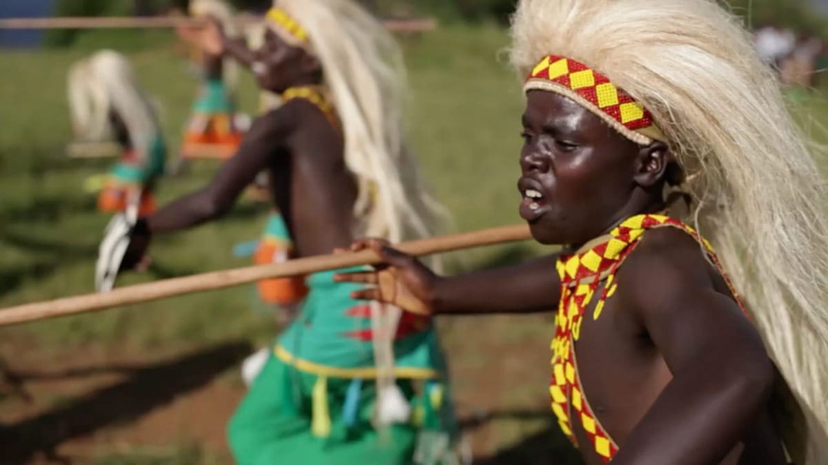 Intore Dancers with vibrant costumes and white headdresses performing for 'The Magical Virungas' video by Volcanoes Safaris.