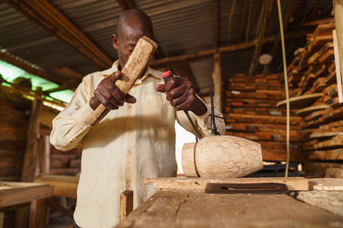 Local artisan skillfully carving wood at Volcanoes Safaris' Kibale Lodge, showcasing the intricate craftsmanship contributing to the lodge's authentic decor.