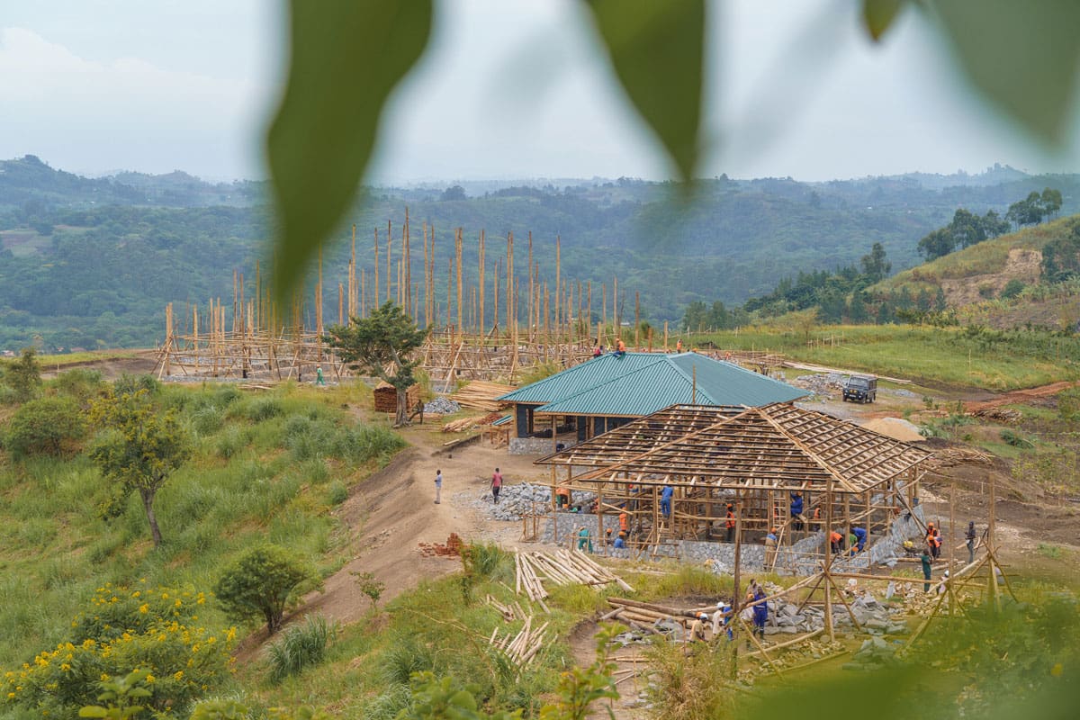 Elevated view of the active construction site at Volcanoes Safaris' Kibale Lodge, with workers assembling the structural framework amidst the greenery of Uganda's landscapes.