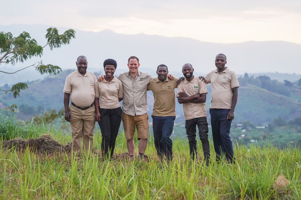 Team members of Volcanoes Safaris, including COO Kevin James, botanist Celine, construction manager Cyprien Serugero, and construction team members, stand together amidst the greenery near the Kibale Lodge site, showcasing the collaboration behind the creation of this eco-friendly retreat.