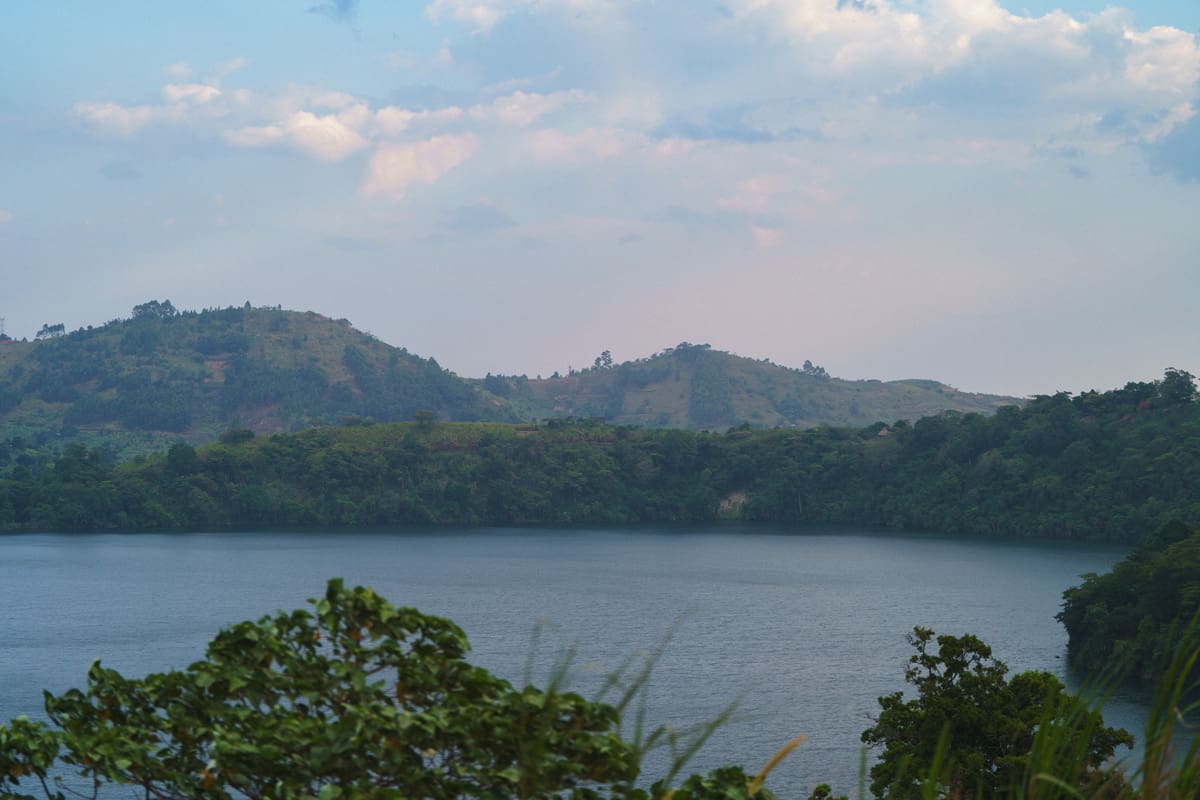Tranquil waters of a crater lake nestled among the rolling hills near the site of the Volcanoes Safaris' Kibale Lodge, capturing the serene beauty of Uganda's landscapes.