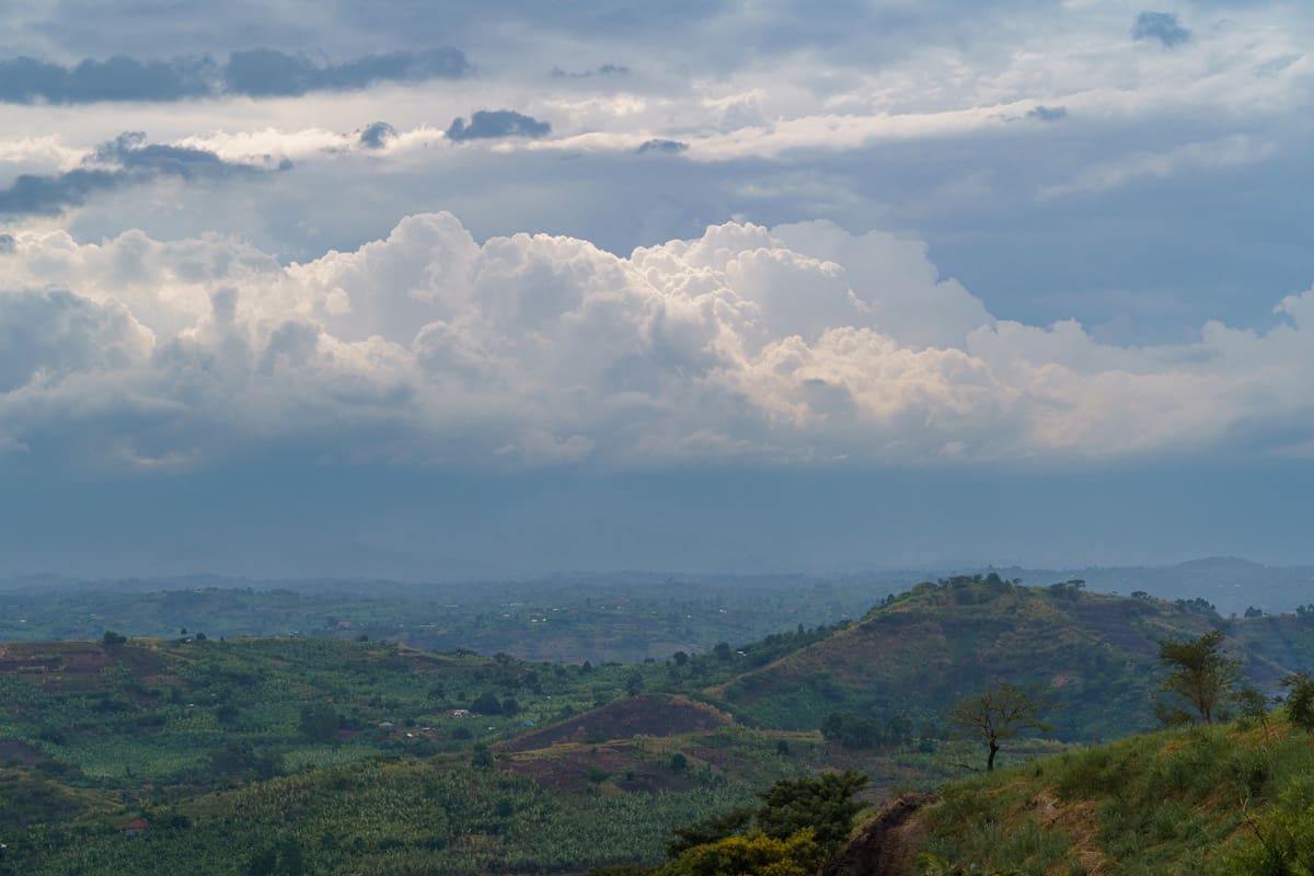 Majestic clouds over the lush green undulating hills near Volcanoes Safaris' Kibale Lodge in Uganda, showcasing the region's natural splendor.